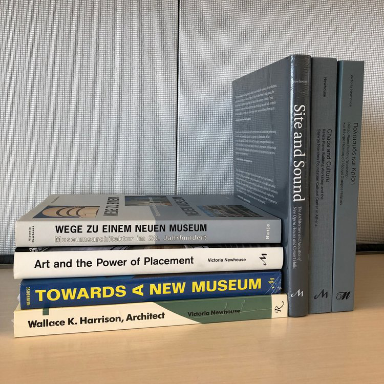 A stack of white, gray, and a blue books with the titles: Wallack K. Harrison Architect, Towards A New Museum, Art and the Power of Placement, Site and Sound, and Chaos and Culture. 2 books are in German.